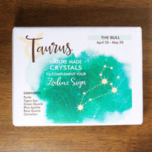 Load image into Gallery viewer, A box of Taurus natural made crystals to complement your zodiac sign, from Rock Paradise, on a wood background. The box is white with a splatter of green, and the taurus constellation.