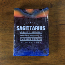 Load image into Gallery viewer, Whiskey Rivers Soap Co. Sagittarius Astrology Soap. The bar is dark purple with orange and blue marbled into the top. In white writing, says "a soap for Sagittarius. November 22-December 21. Smells like a disappearing act. Wandering White Tea."."