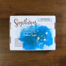 Load image into Gallery viewer, Sagittarius Horoscope Crystals from Rock Paradise. Photo shows a white box that has a blue ink blot with the Sagittarius constellation and illustrations of gemstones. The box reads "Sagittarius nature made crystals to complement your zodiac sign. The Archer. November 22-December 21. Contents: Sodalite, amethyst, orange calcite, pink tourmaline, crystal quartz, smoky quartz."