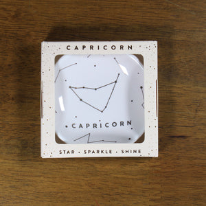 Capricorn Zodiac Ring Dish from Lucky Feather. Cream colored ring dish with gold print. Ring dish says Capricorn and has an illustration of the Capricorn constellation.