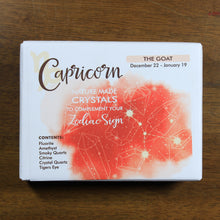 Load image into Gallery viewer, Capricorn Horoscope Crystals from Rock Paradise. Photo shows a white box that has a coral colored ink blot with the Capricorn constellation and illustrations of gemstones. The box reads "Capricorn nature made crystals to complement your zodiac sign. The Goat. December 22-January 19. Contents: Fluorite, Amethyst, Smoky Quartz, Citrine, Crystal Quartz, Tigers Eye."