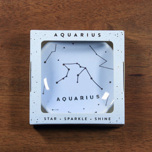 Aquarius Zodiac Ring Dish from Lucky Feather. Light blue colored ring dish with gold print. Ring dish says Aquarius and has an illustration of the Aquarius constellation.