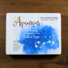 Load image into Gallery viewer, Aquarius Horoscope Crystals from Rock Paradise. Photo shows a white box that has a blue colored ink blot with the Aquarius constellation and illustrations of gemstones. The box reads " Aquarius nature made crystals to complement your zodiac sign. The Water Carrier. January 20-February 18. Contents: Hematite, Amethyst, Crystal Quartz, Blue Apatite, Rose Quartz, Fluorite."