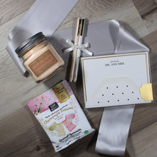 Load image into Gallery viewer, Overhead view of Dearly Beloved wedding gift box items: candle, gummie bears, felt pens, and note cards over silver ribbon