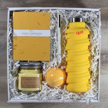 Load image into Gallery viewer, An overhead shot of the "You're The Zest" yellow themed gift box, which includes a yellow journal, a white pen, a yellow water bottle, a yellow bath bomb, and a yellow candle all in a white box with white crinkle paper