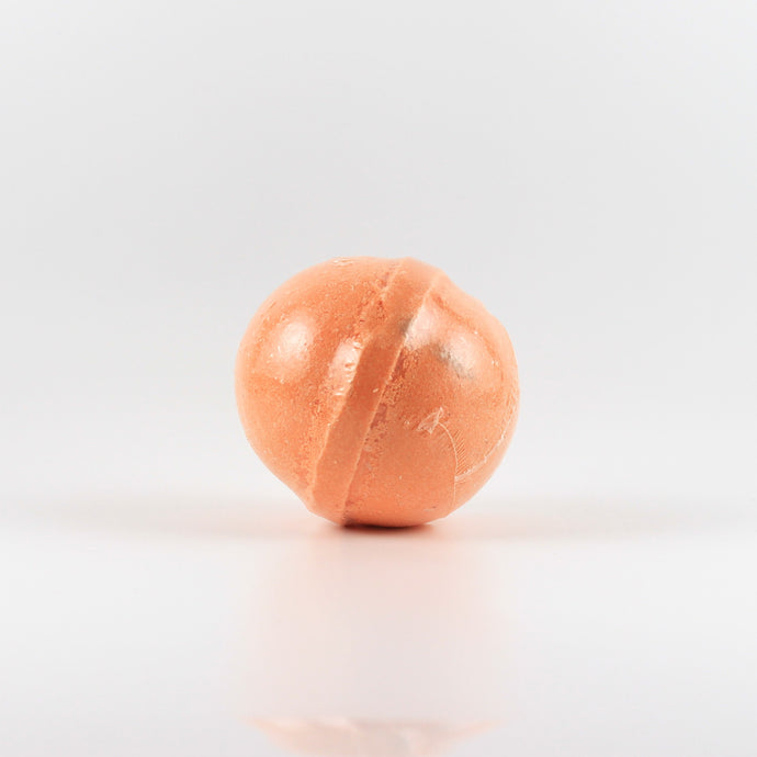 An orange colored, oval shaped bath bomb on a white background