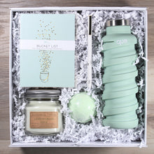 Load image into Gallery viewer, Overhead view of the "For Your Enjoy-Mint" gift box, which includes a light green water bottle, a light green bath bomb, a white pen with gold accents, a mason jar candle with green wax, and a light green journal that says "bucket list", all in a white box with white crinkle paper