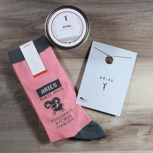Load image into Gallery viewer, contents of astrology gift box on wood background, including pink socks, gold pendant necklace, tin candle