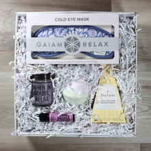 Load image into Gallery viewer, Overhead view of the "Major Chill Pill" gift box with a tea pyramid, a candle, an eye mask, an aromatherapy roller, and  a bath bomb, all in a white box with white crinkle paper
