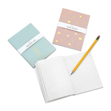 Load image into Gallery viewer, This photo shows two closed journals (one pink "love notes" journal and one green "bucket list" journal) next to a third open journal with blank pages and a yellow pencil laying across it.