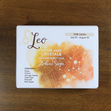 Load image into Gallery viewer, Leo Horoscope Crystals from Rock Paradise. Photo shows a white box that has a orange colored ink blot with the Leo constellation and illustrations of gemstones. The box reads " Leo nature made crystals to complement your zodiac sign. The Lion. July 23-August 22. Contents: Pyrite, Citrine, Orange Calcite, Tigers Eye, Emerald, Red Jasper."