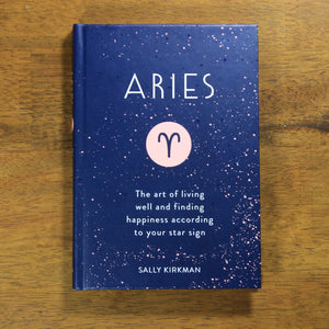 overhead view of book: "Aries: The art of living well and finding happiness according to your star sign" by Sally Kirkman. The cover has the title, author, and the Aries zodiac symbol in a pink circle