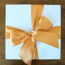 Load image into Gallery viewer, This photo is an overhead view of white gift box with butterscotch orange satin ribbon tied in a bow, on top of a wood table