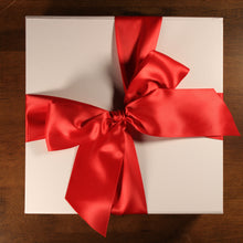 Load image into Gallery viewer, This photo shows an overhead view of white gift box with red satin ribbon tied in a bow, on top of a wood table