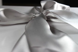 Close up side view of a silver satin bow on a white box