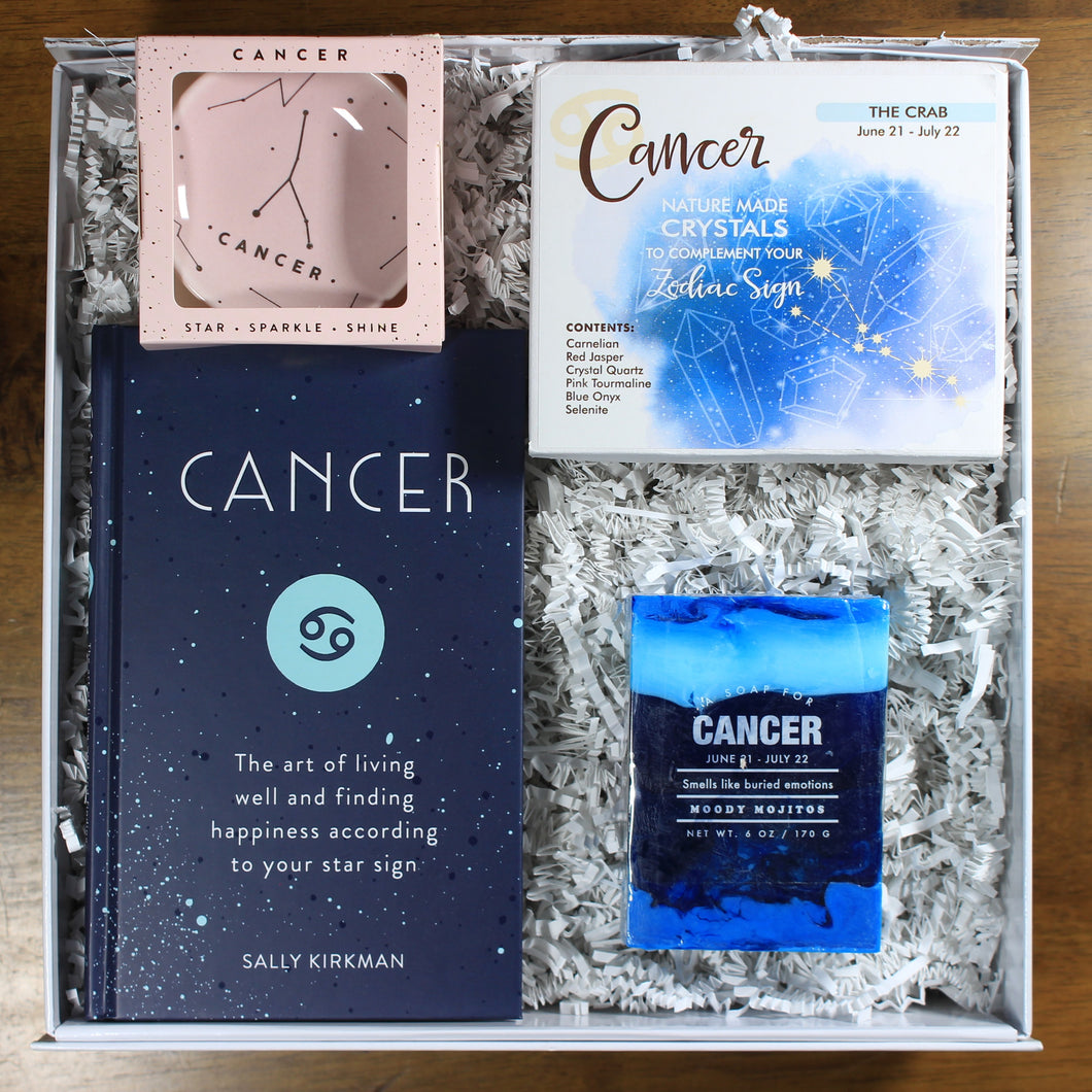 What's Your Sign Cancer Gift Box: photo shows a white gift box with crinkle paper, filled with a Cancer book, Cancer ring dish, Cancer crystals, and Cancer soap.