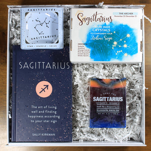 What's Your Sign Sagittarius Gift Box: photo shows a white gift box with crinkle paper, filled with a sagittarius book, sagittarius ring dish, sagittarius crystals, and sagittarius soap.