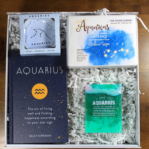 What's Your Sign Aquarius Gift Box: photo shows a white gift box with crinkle paper, filled with a Aquarius book, Aquarius ring dish, Aquarius crystals, and Aquarius soap.