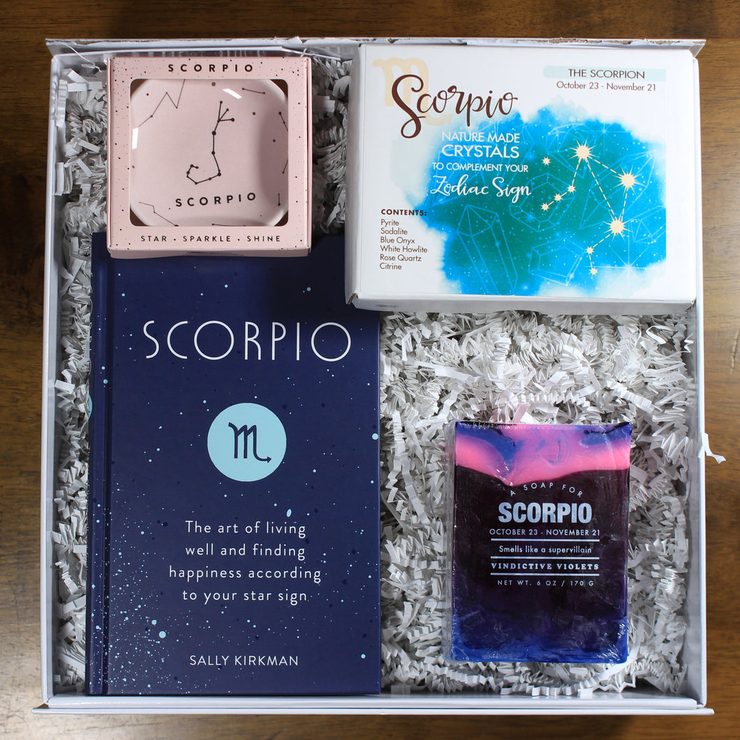 What's Your Sign Scorpio Gift Box: photo shows a white gift box with crinkle paper, filled with a Scorpio book, scorpio ring dish, scorpio crystals, and scorpio soap.