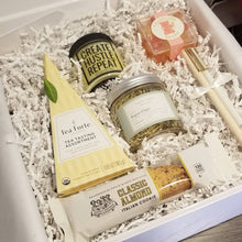 Load image into Gallery viewer, This photo shows a custom Doromania gift box with a yellow tea pyriamid, a single almond biscotti, a jar of gold paper clips, a yellow candle, pink champagne gummy bears, and two pens all in a white box with white crinkle paper.
