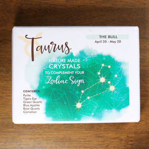 A box of Taurus natural made crystals to complement your zodiac sign, from Rock Paradise, on a wood background. The box is white with a splatter of green, and the taurus constellation.