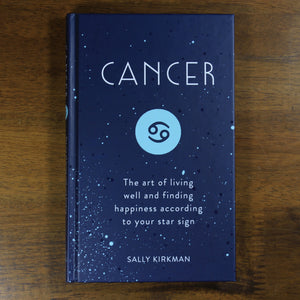 A dark blue book titled Cancer: The art of living well and finding happiness according to your star sign. The book is by Sally Kirkman. The cover has the title, author, and the Cancer zodiac symbol in a light blue circle.