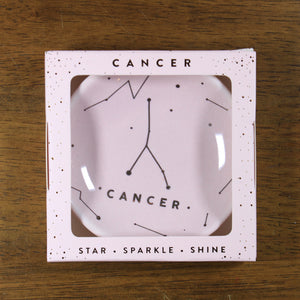 Cancer Zodiac Ring Dish from Lucky Feather. Blush colored ring dish with gold print. Ring dish says Cancer and has an illustration of the Cancer constellation.