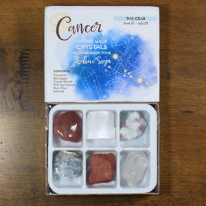 ancer Horoscope Crystals from Rock Paradise. Photo shows a white box that has a blue colored ink blot with the Cancer constellation and illustrations of gemstones. The box reads "Cancer nature made crystals to complement your zodiac sign. The Crab. June 21-July 22. Contents: Carnelian, Red Jasper, Crystal Quartz, Pink Tourmaline, Blue Onyx, Selenite."