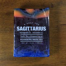 Load image into Gallery viewer, Whiskey Rivers Soap Co. Sagittarius Astrology Soap. The bar is dark purple with orange and blue marbled into the top. In white writing, says &quot;a soap for Sagittarius. November 22-December 21. Smells like a disappearing act. Wandering White Tea.&quot;.&quot;