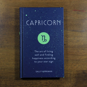 A dark blue book titled Capricorn: The art of living well and finding happiness according to your star sign. The book is by Sally Kirkman. The cover has the title, author, and the Capricorn zodiac symbol in a green circle.
