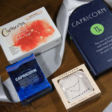 Load image into Gallery viewer, Photo shows the contents of the What&#39;s Your Sign Capricorn Gift Box: Capricorn book, Capricorn ring dish, Capricorn crystals, and Capricorn soap. Items are laid over a silver ribbon.