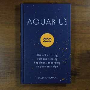A dark blue book titled Aquarius: The art of living well and finding happiness according to your star sign. The book is by Sally Kirkman. The cover has the title, author, and the Aquarius zodiac symbol in a yellow circle.