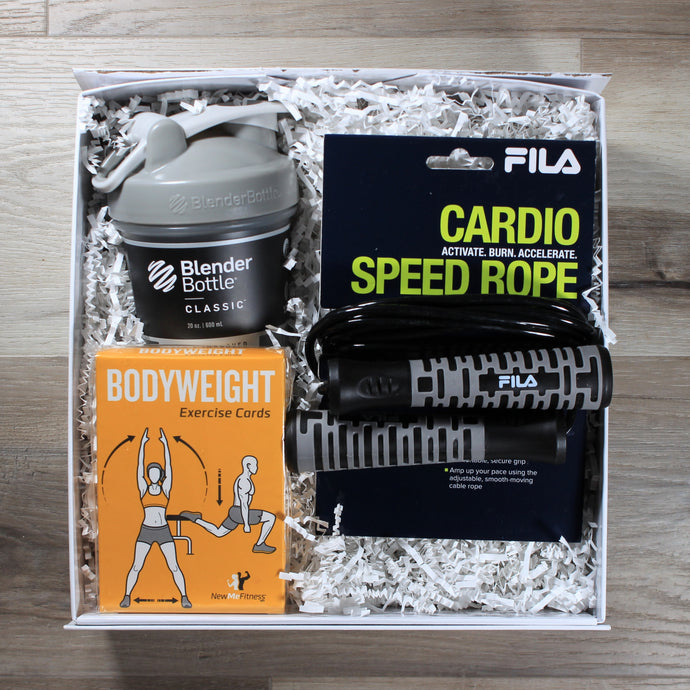 This photo shows an overhead shot of the Reps and Ropes gift box from Doromania, which includes a bottle with a grey lid, a black jump rope with grey handles, and a yellow box of exercise cards, all in a white gift box with white crinkle paper
