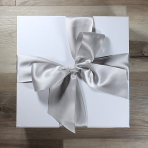overhead view of white gift box with silver satin ribbon tied in a bow