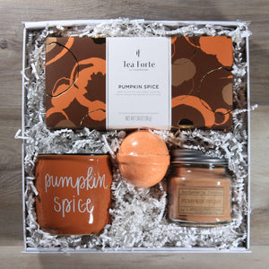 Overhead view of the "Pumpkin Spice Everything" gift box with a box of pumpkin spice tea, an orange pumpkin spice mug, and orange pumpkin spice bath bomb, and a brown pumpkin pecan candle, all in a white box with white crinkle paper