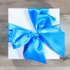 An overhead view of a white magnetic square gift box with a teal satin ribbon tied in a bow