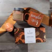 Load image into Gallery viewer, Flat lay of pumpkin spice everything gift box contents: a brown pumpkin pecan candle, an orange pumpkin spice mug, and orange pumpkin spice bath bomb, and a box of pumpkin spice tea, and a butterscotch colored ribbon