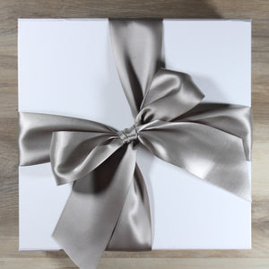 White square gift box with a grey satin bow, on a wood background