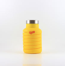 Load image into Gallery viewer, A photo of the compressed version of an expandable citrus yellow water bottle with a metal cap, that says &quot;que&quot; in pink lowercase letters.