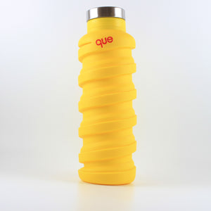 A photo of a yellow bottle with a metal cap that says "que" in pink; the bottle has a spiral design.