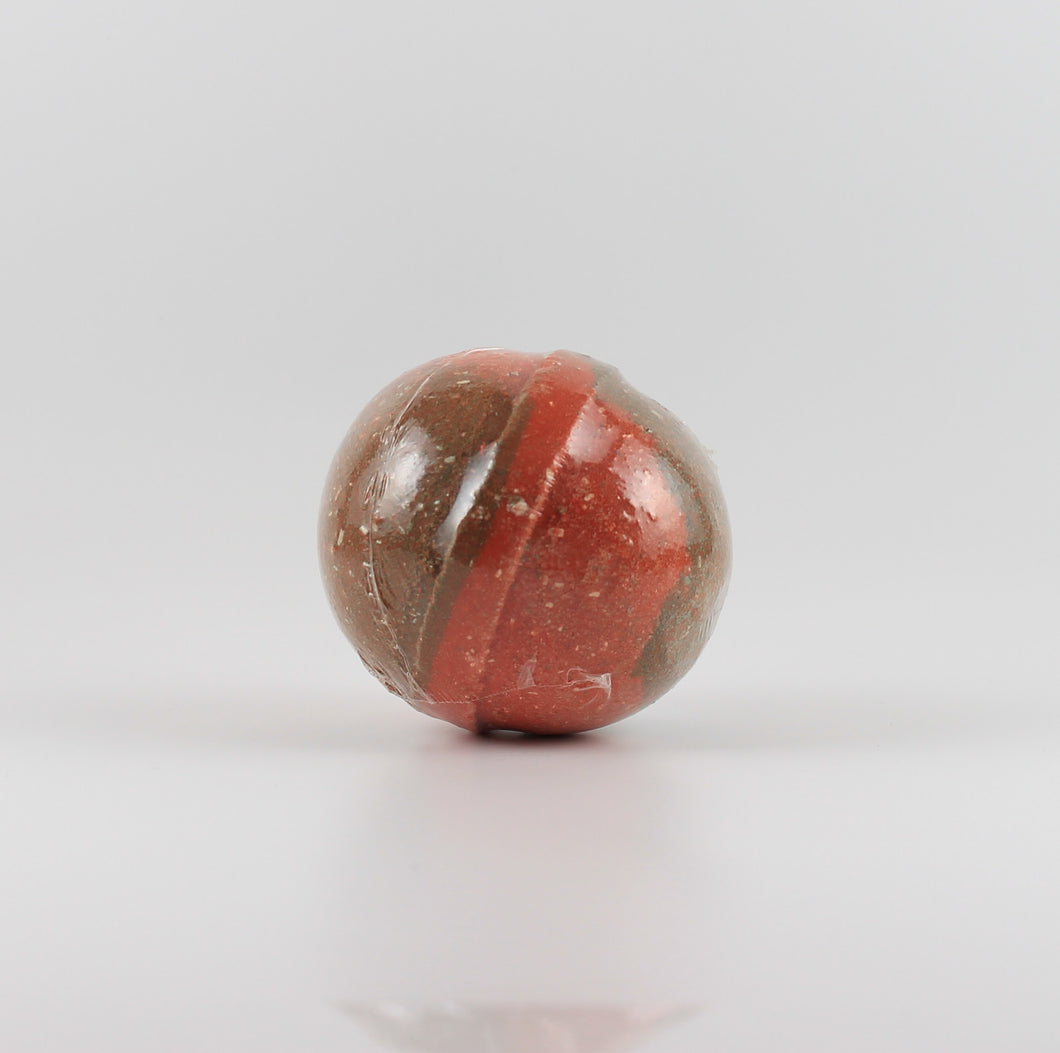A brown and red colored, oval shaped bath bomb on a white background