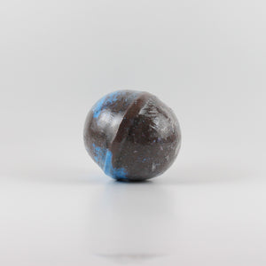 A mostly black colored, oval shaped bath bomb with splashes of blue on a white background