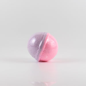 A pink and purple colored, oval shaped bath bomb on a white background. Exactly half is purple and half is pink.