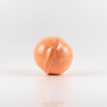 Load image into Gallery viewer, An orange colored, oval shaped bath bomb on a white background