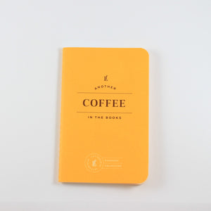 Small yellow passport journal from Letterfolk with gold print that says "Another coffee in the books"