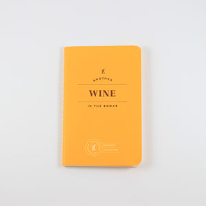 Small yellow passport journal from Letterfolk with gold print that says "Another wine in the books"