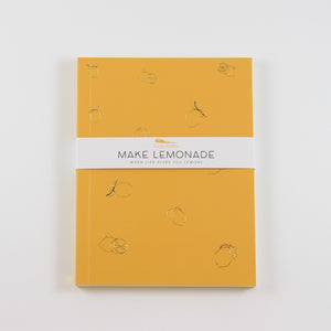 A photo of a rectangle journal with lemons etched on the cover. A paper band around the outside says "Make Lemonade"