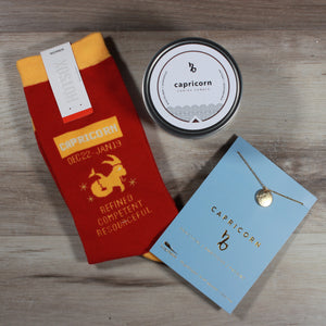 Flat lay photo of the contents of the A Little Bit Capricorn gift box: Capricorn candle, Capricorn socks, and a Capricorn Necklace. A fun horoscope gift for friends.