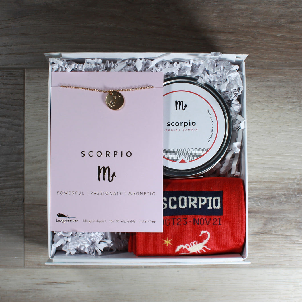small Scorpio gift box from Doromania. Box includes a Scorpio disc necklace, a Scorpio candle, and Scorpio socks. These gifts are packaged in a white gift box with white crinkle paper.