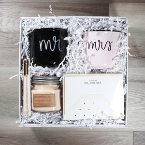 overhead view of "Mr & Mrs" wedding gift box with candle, two mugs, note cards, and felt pens in a white box with white crinkle paper